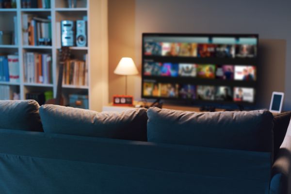 Una televisione accesa in salotto su una piattaforma di programmi tv on demand, con accanto una lampada accesa.