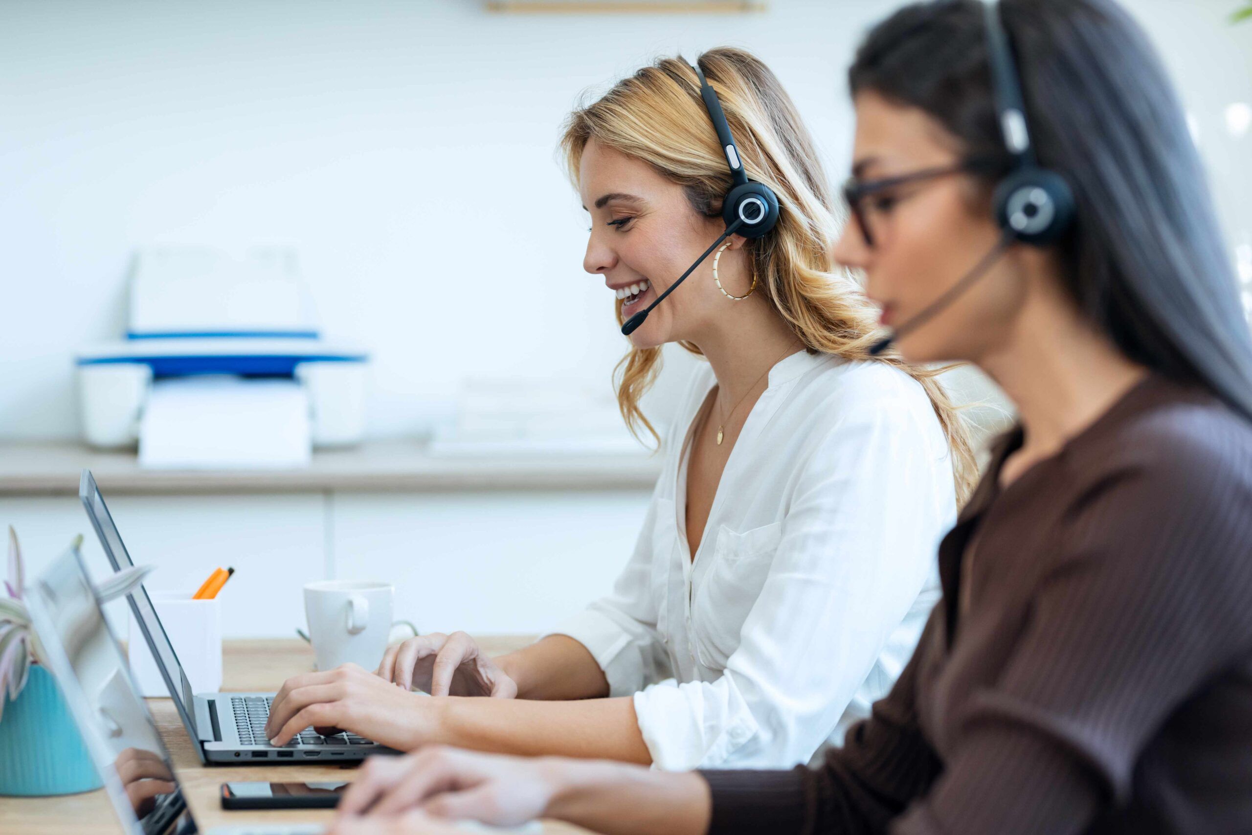 Due addette al customer service, sedute davanti al computer, rispondo alle chiamate tramite le loro cuffie.