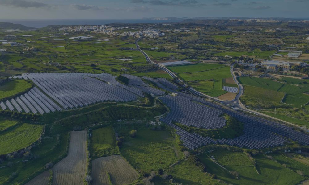 Vista aerea di una collina ricoperta da un campo fotovoltaico con sullo sfondo una città.