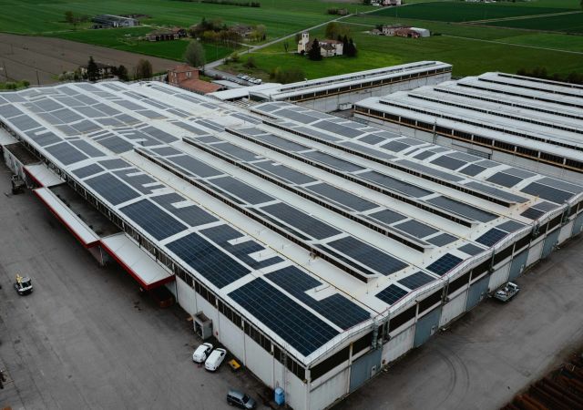 Un tecnico con regolari DPI sta posizionando un pannello fotovoltaico in mezzo ad altri pannelli.
