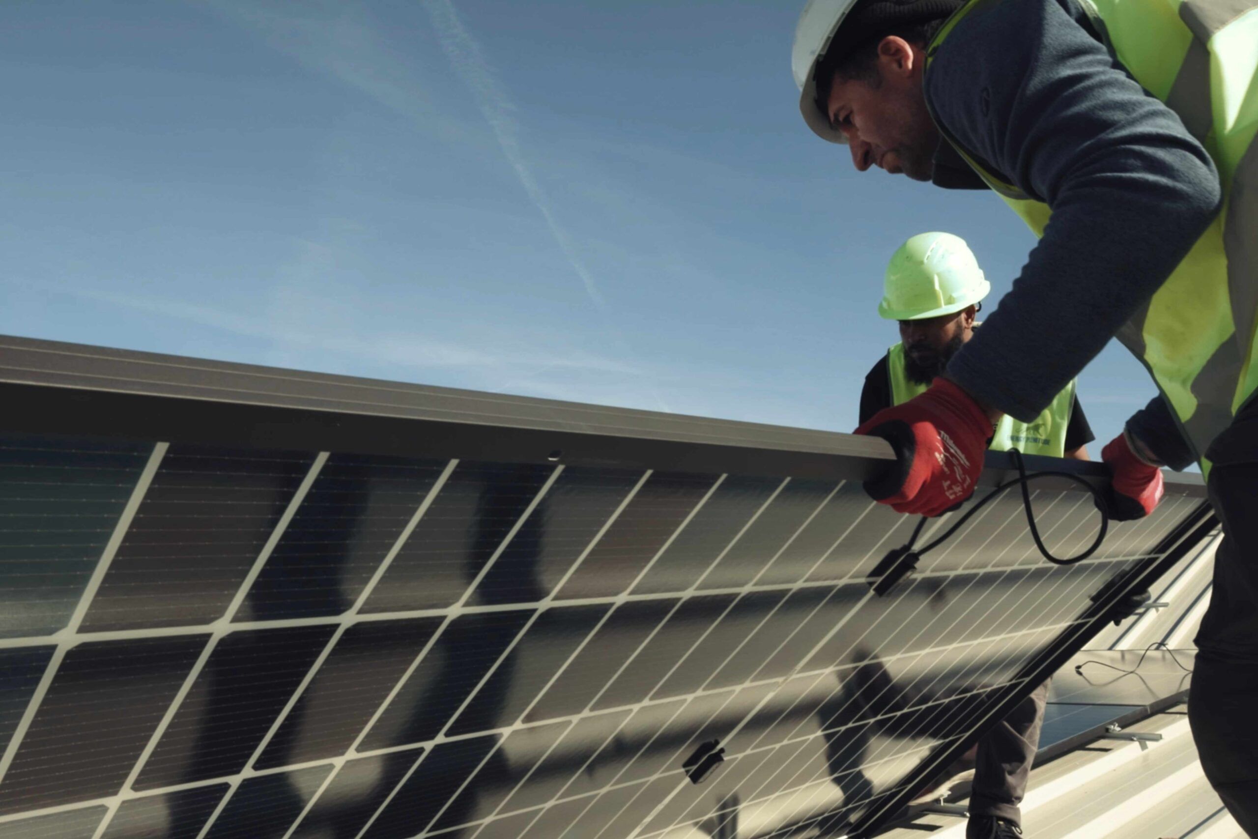Un tecnico con regolari DPI sta posizionando un pannello fotovoltaico in mezzo ad altri pannelli.