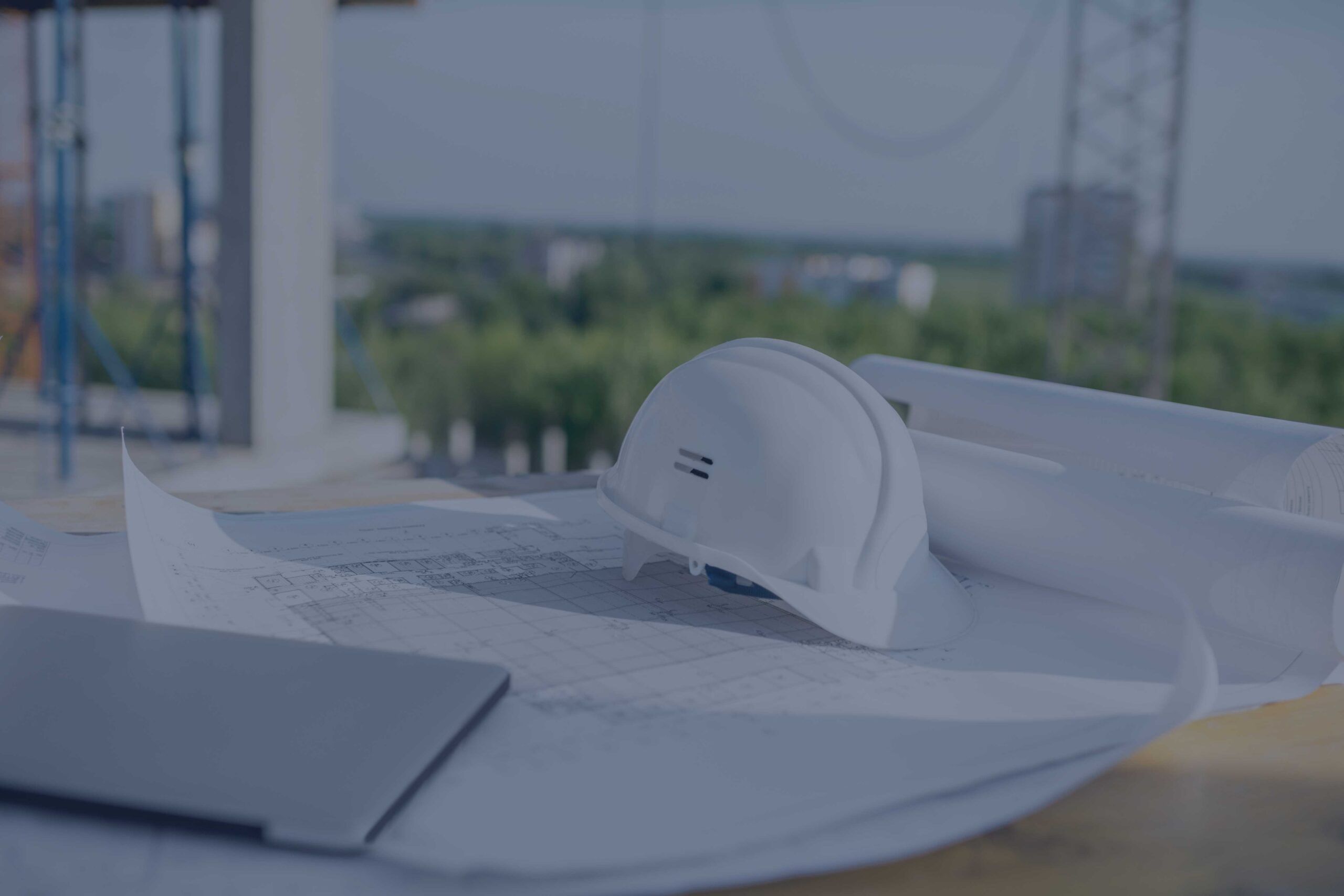 Un caschetto bianco da cantiere appoggiato su una planimetria semi avvolta adagiata su un tavolo da lavoro in un cantiere.